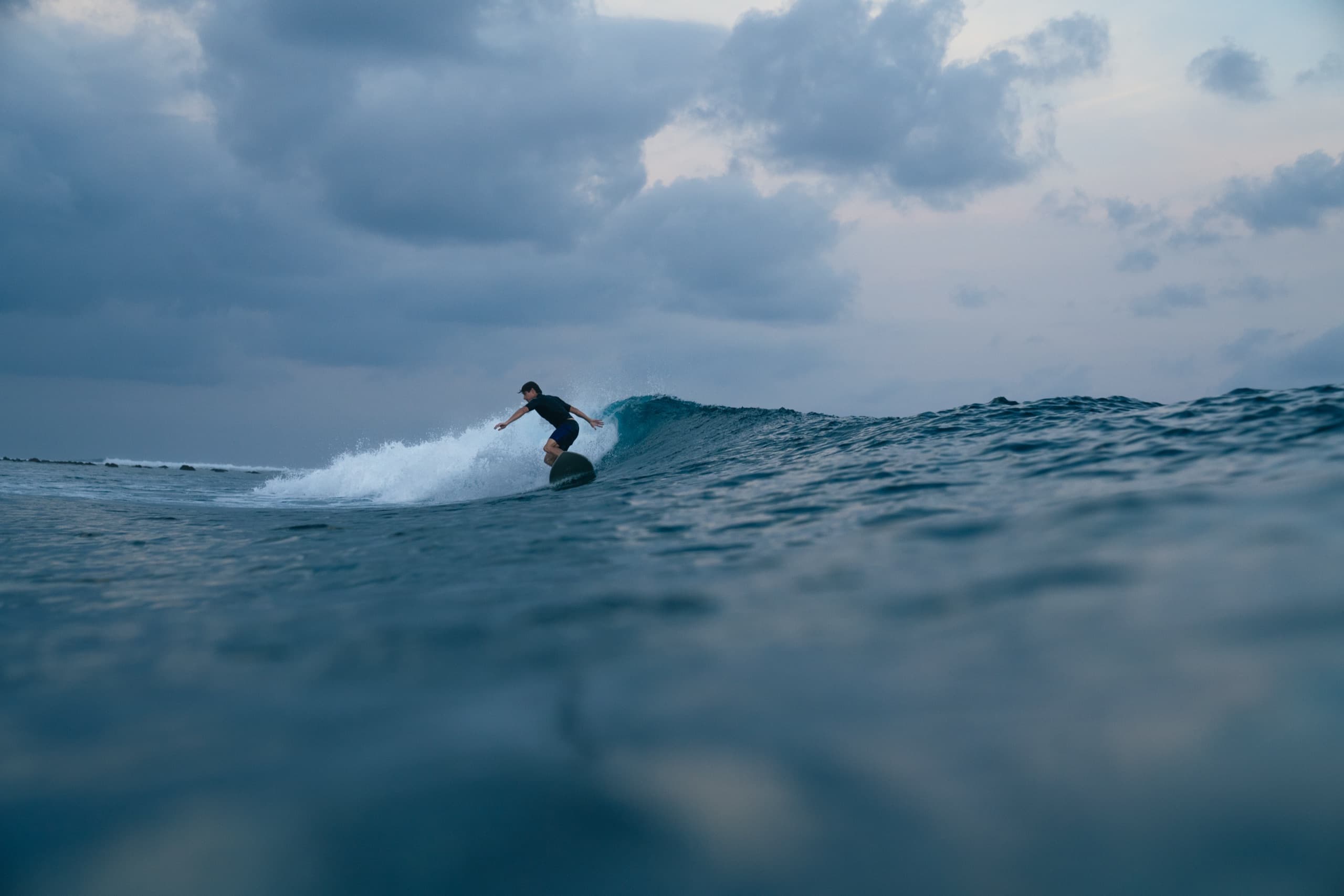 Surfer carving a wave under heavy grey clouds, seen from water level